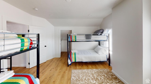 bedroom featuring light wood-style flooring, vaulted ceiling, and baseboards
