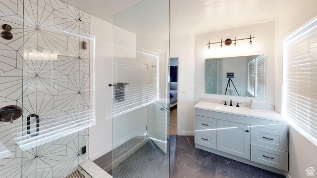 full bathroom with marble tiled flooring, a tile shower, and vanity
