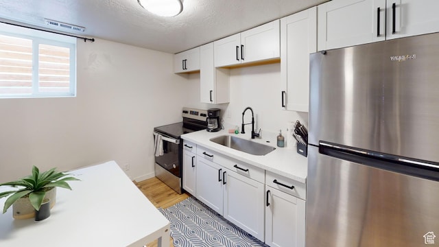 kitchen with appliances with stainless steel finishes, a sink, light countertops, white cabinets, and a textured ceiling