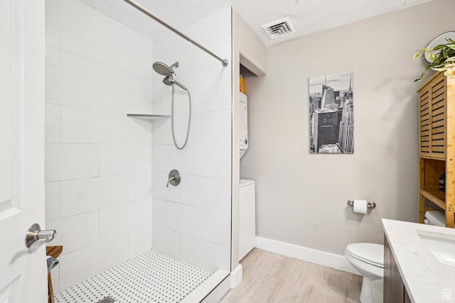 bathroom featuring stacked washer / dryer, a tile shower, toilet, vanity, and baseboards