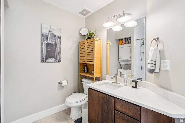 bathroom featuring stacked washing machine and dryer, toilet, vanity, and baseboards