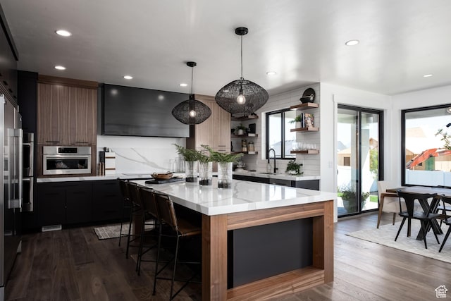 kitchen with open shelves, appliances with stainless steel finishes, a sink, a kitchen island, and a kitchen bar