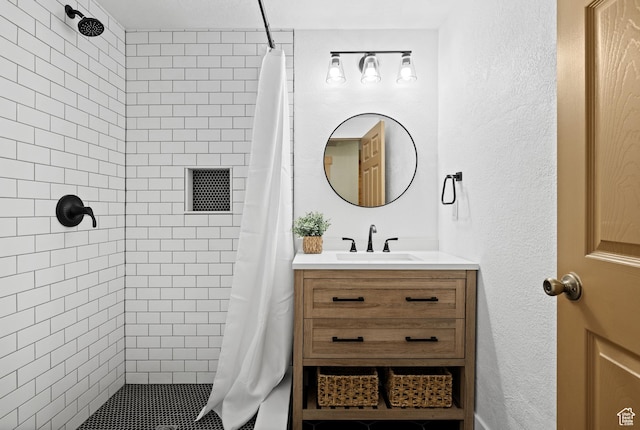 bathroom with a tile shower, vanity, and a textured wall
