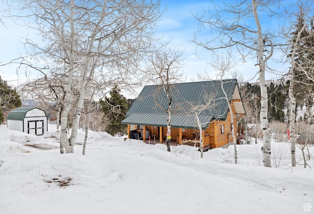 snow covered back of property with a storage shed, an outbuilding, and metal roof