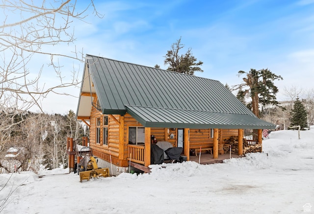 snow covered property with covered porch, log exterior, metal roof, and a standing seam roof
