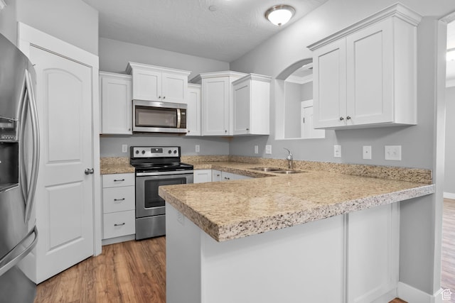 kitchen with appliances with stainless steel finishes, a peninsula, a sink, and wood finished floors