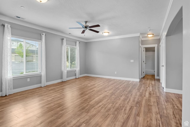 empty room featuring arched walkways, plenty of natural light, ceiling fan, light wood-style floors, and crown molding