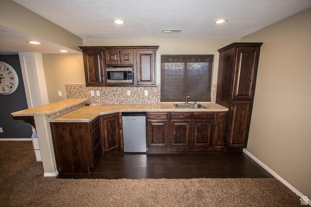 kitchen with stainless steel appliances, a sink, a peninsula, light countertops, and recessed lighting