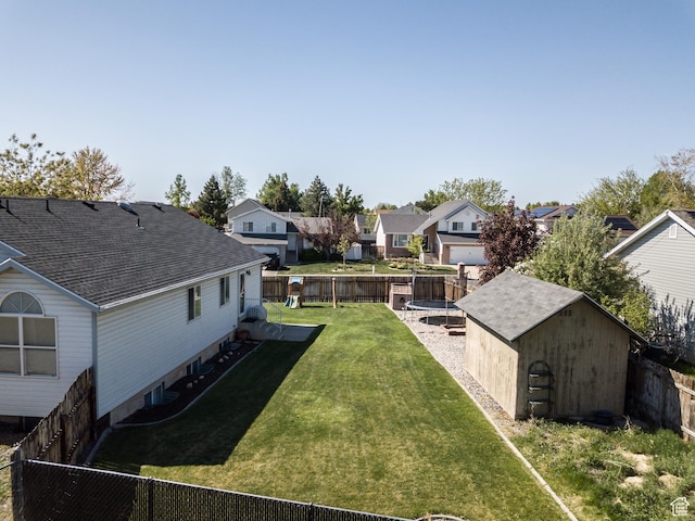 view of yard with a trampoline, a storage unit, a residential view, and an outbuilding