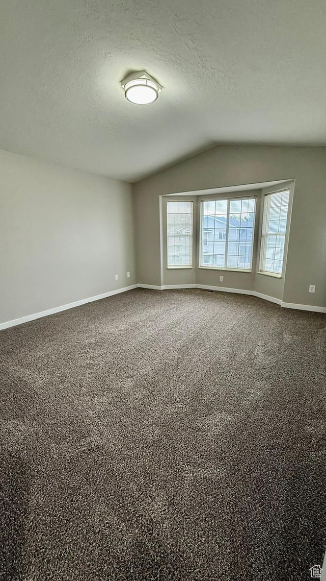 unfurnished room featuring lofted ceiling, baseboards, a textured ceiling, and dark colored carpet