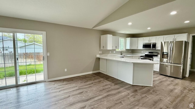 kitchen featuring appliances with stainless steel finishes, healthy amount of natural light, a peninsula, a sink, and vaulted ceiling