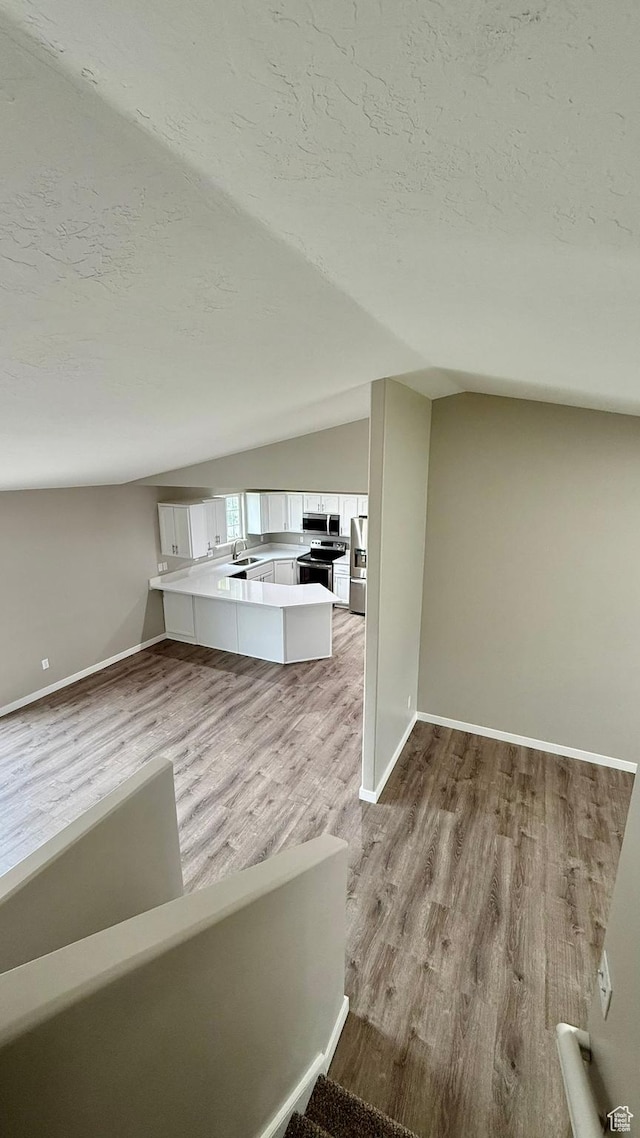 unfurnished living room with lofted ceiling, wood finished floors, a textured ceiling, a sink, and baseboards