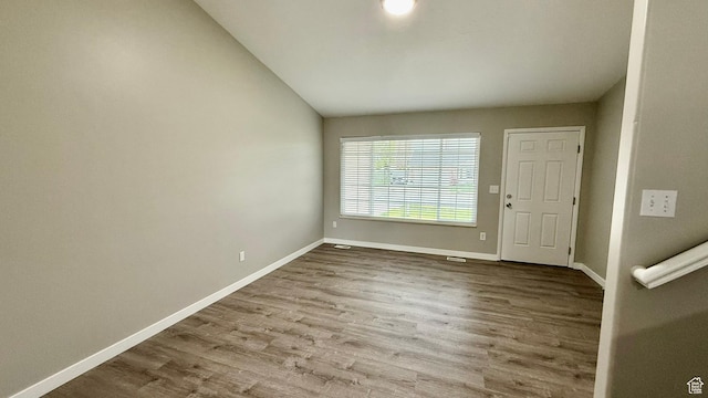 empty room featuring lofted ceiling, wood finished floors, and baseboards