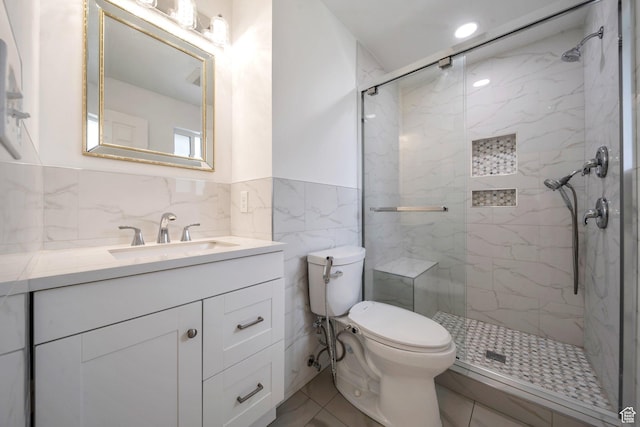 full bathroom with a marble finish shower, vanity, tile walls, toilet, and a wainscoted wall