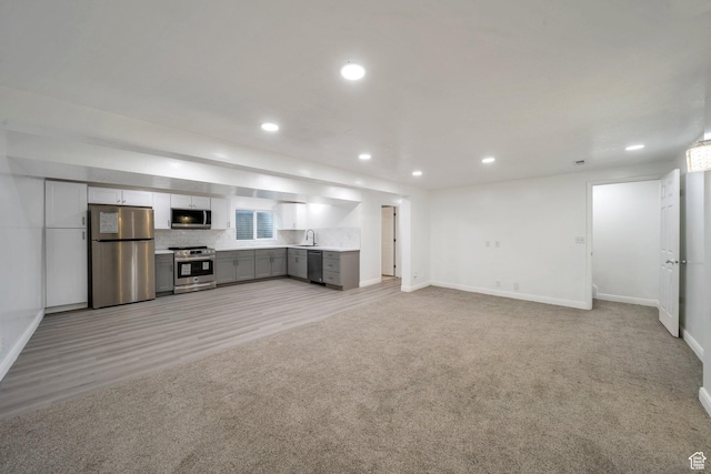 unfurnished living room featuring baseboards, recessed lighting, a sink, light colored carpet, and light wood-type flooring