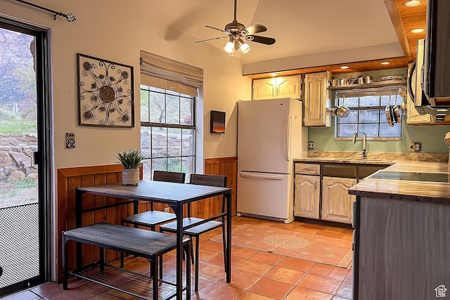 kitchen featuring freestanding refrigerator, a sink, wainscoting, light tile patterned flooring, and a ceiling fan