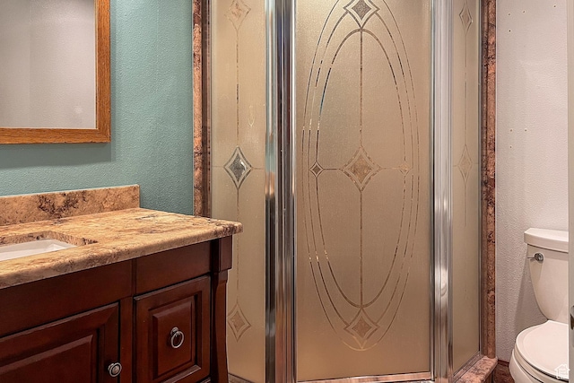 bathroom featuring toilet, a textured wall, a stall shower, and vanity