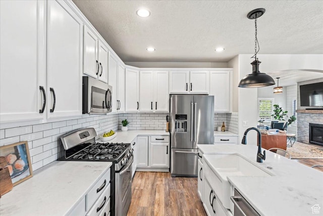 5153 W Bowstring Way S, Jordan, UT 84009 - kitchen with stainless steel appliances, white cabinets, a stone fireplace, a textured ceiling, and recessed lighting
