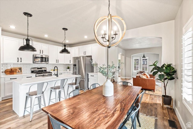 5153 W Bowstring Way S, Jordan, UT 84009 - dining space with a chandelier, arched walkways, light wood-type flooring, plenty of natural light, and recessed lighting
