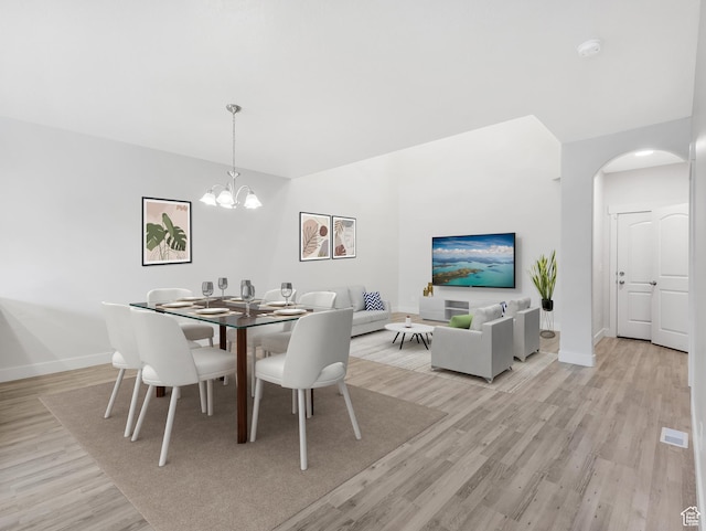 dining area featuring light wood-style floors, arched walkways, baseboards, and a chandelier
