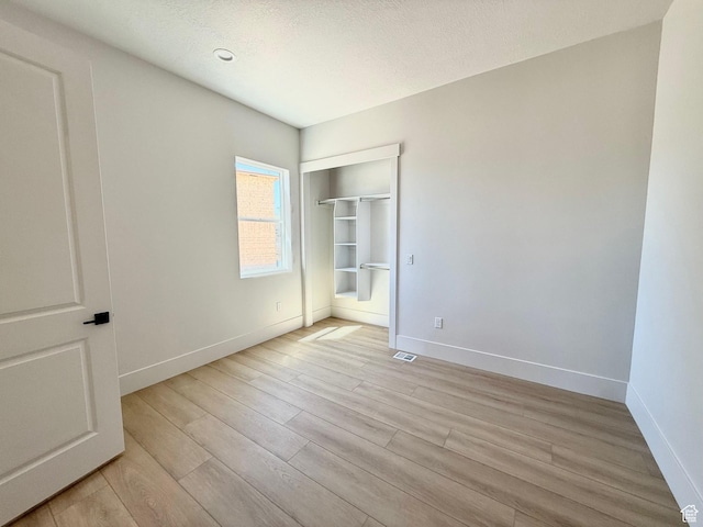 unfurnished bedroom featuring light wood finished floors, baseboards, and a textured ceiling