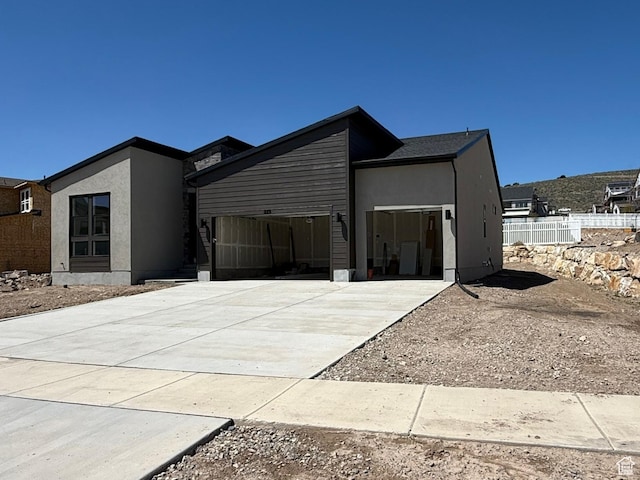 contemporary house with an attached garage, driveway, fence, and stucco siding