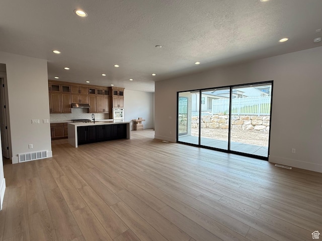 unfurnished living room featuring recessed lighting, a textured ceiling, light wood-style flooring, and baseboards