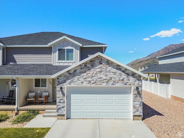 view of front of house with stone siding, a porch, driveway, and fence