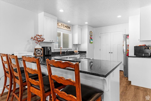 kitchen featuring a kitchen bar, freestanding refrigerator, dark wood-style floors, a sink, and white cabinets