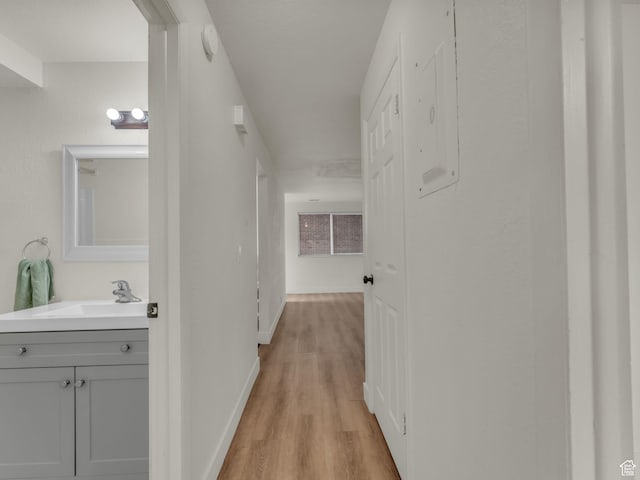 corridor with a sink, light wood-type flooring, and baseboards