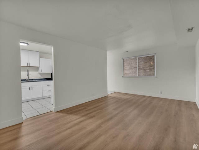unfurnished room featuring light wood-style floors, a sink, and baseboards