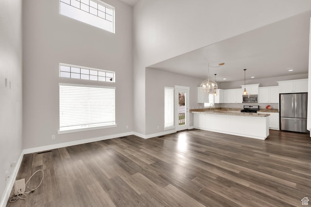 unfurnished living room featuring dark wood-type flooring, baseboards, a towering ceiling, a chandelier, and recessed lighting