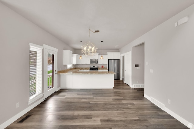 kitchen with appliances with stainless steel finishes, a peninsula, a chandelier, white cabinetry, and baseboards