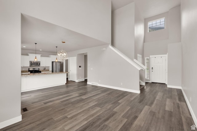 unfurnished living room featuring a high ceiling, dark wood-type flooring, a chandelier, baseboards, and stairway