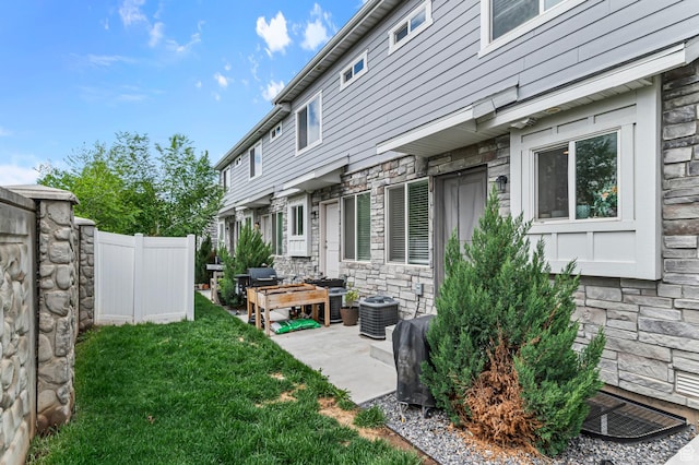 view of side of property featuring stone siding, cooling unit, and a patio