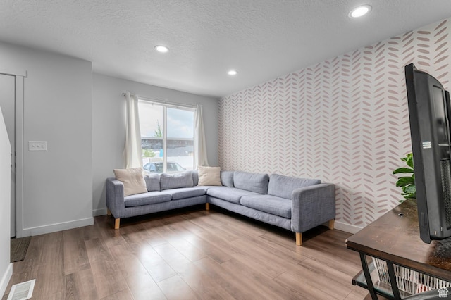 living room featuring wallpapered walls, an accent wall, baseboards, recessed lighting, and a textured ceiling