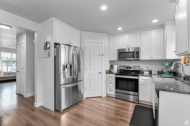 kitchen featuring appliances with stainless steel finishes, a sink, wood finished floors, white cabinets, and dark stone counters