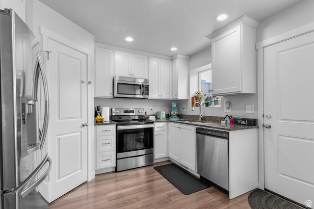 kitchen with appliances with stainless steel finishes, a sink, recessed lighting, white cabinets, and light wood-style floors