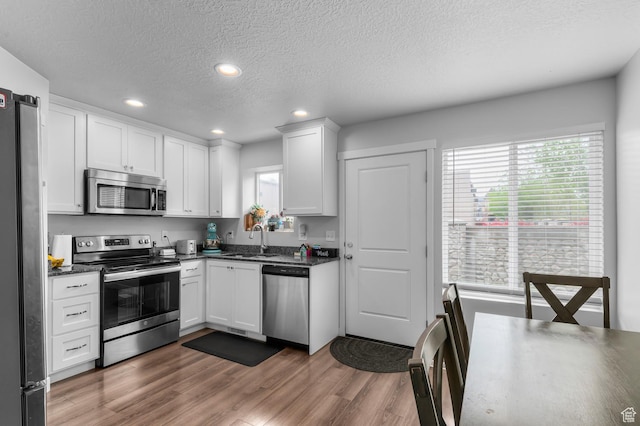 kitchen featuring stainless steel appliances, a sink, a textured ceiling, white cabinets, and recessed lighting