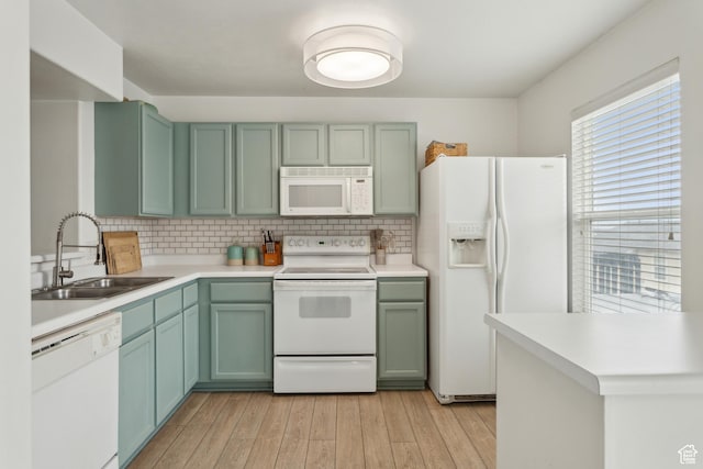 kitchen with white appliances, a sink, green cabinetry, and light wood finished floors