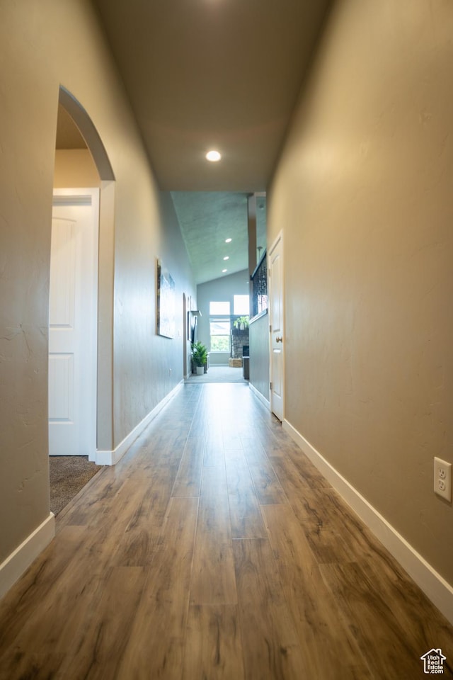 corridor featuring baseboards, wood finished floors, vaulted ceiling, arched walkways, and recessed lighting