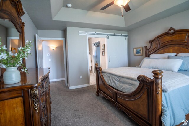 bedroom featuring a tray ceiling, carpet, a barn door, and baseboards