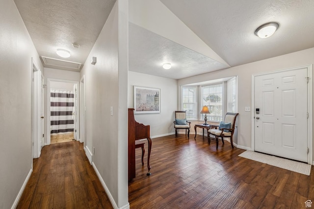 foyer entrance featuring a textured ceiling, dark wood-type flooring, and baseboards