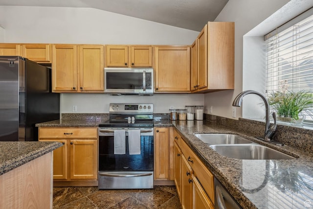 kitchen with stainless steel appliances, vaulted ceiling, a sink, dark stone counters, and dark stone finish floors