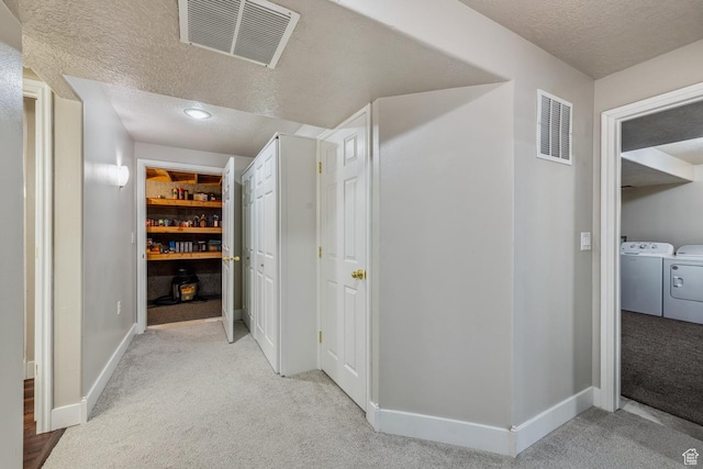 hall with light colored carpet, washer and dryer, a textured ceiling, and baseboards