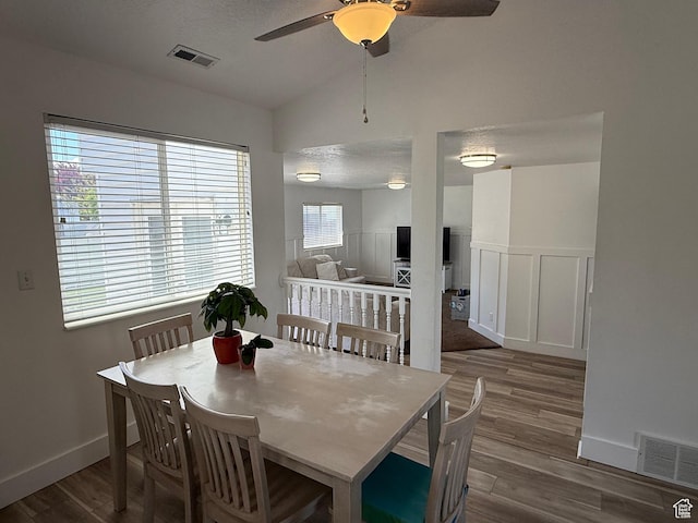 dining room featuring wood finished floors, lofted ceiling, a ceiling fan, wainscoting, and a decorative wall