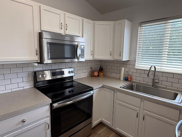 kitchen with appliances with stainless steel finishes, a sink, light countertops, white cabinetry, and decorative backsplash