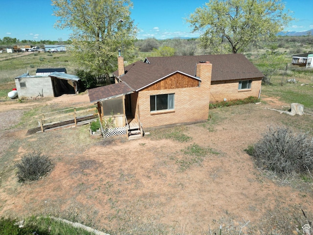 back of property featuring a chimney, brick siding, fence, and roof with shingles