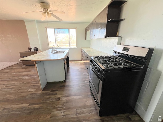 kitchen with gas stove, a sink, dark wood-style floors, light countertops, and a kitchen island with sink