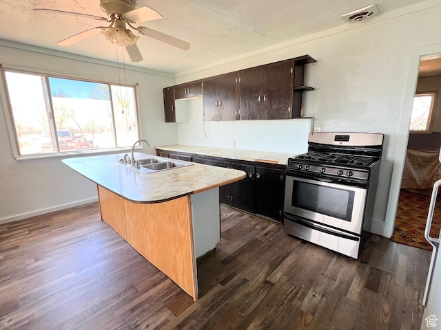 kitchen with stainless steel range with gas cooktop, a sink, light countertops, dark wood finished floors, and plenty of natural light